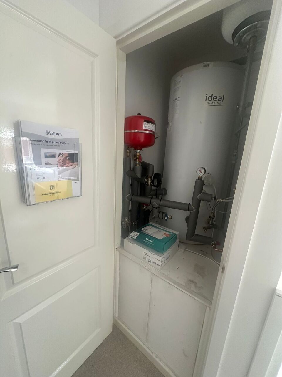 Utility cupboard showing retained Ideal cylinder and heat pump brochure – Darwen new-build Zero Disruption project
