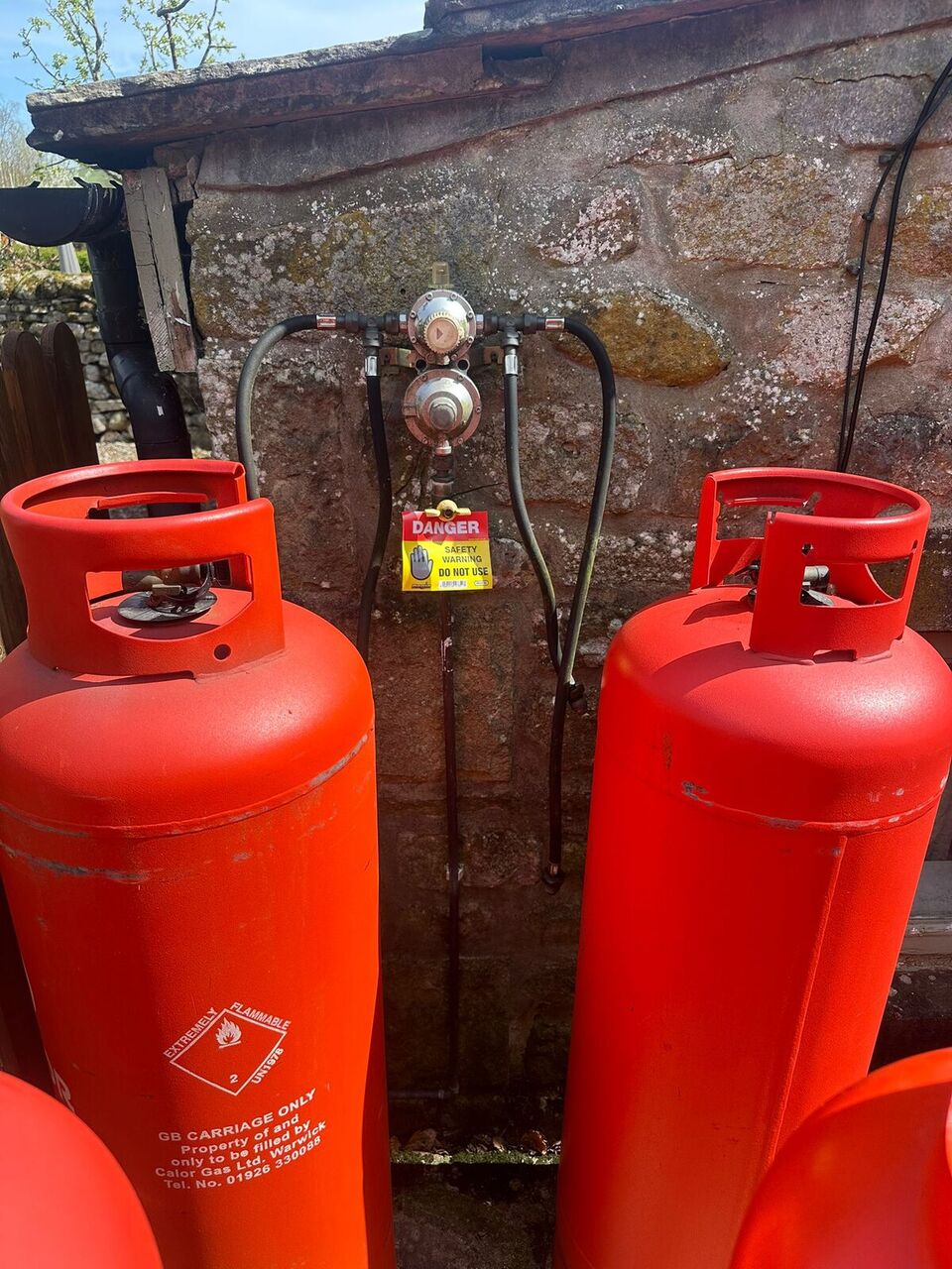 Multiple red LPG cylinders with new regulators, hoses and clear DANGER safety warning labels